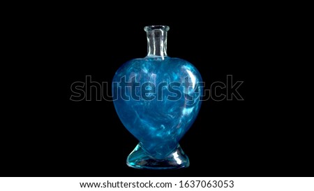 Glass bottle in the form of a heart with blue liquid. The elixir is spinning and overflowing with liquid. Potion of love is isolated on a black background.