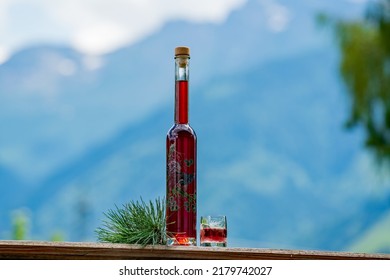 a glass and bottle fresh liquor from the swiss stone pine at a sunny july day with the mountains in the background