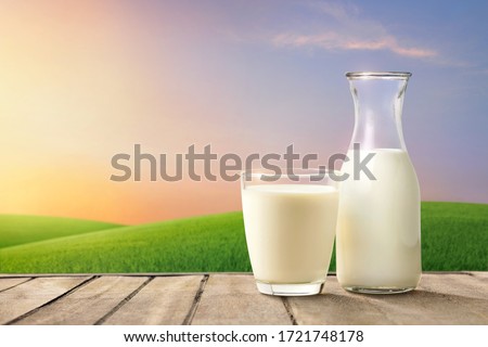Glass and bottle of fresh milk on wooden table with green meadow and mornig light background.