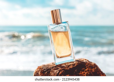 Una botella de vidrio de perfume dorado sobre una carcajada. Las olas del mar al fondo. Concepto de perfume y plantilla de publicidad.