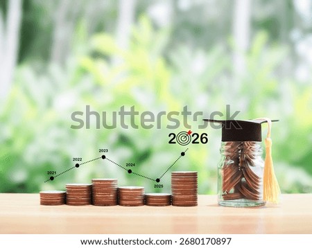 Glass bottle with graduation hat and stack of coins with virtual increasing graph. The concept of saving money for education, student loan, scholarship, tuition fees in year 2026.