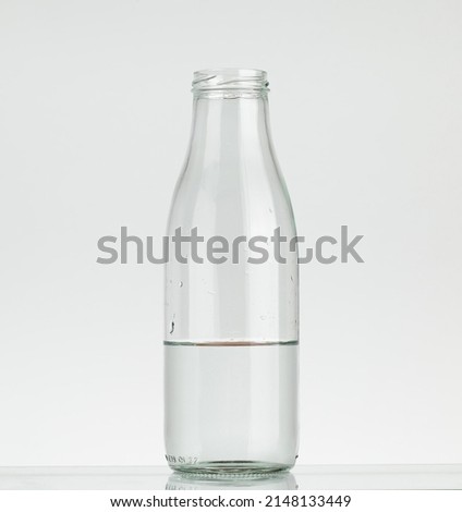 Glass bottle half filled with water. Water bottle without cap isolated on white background.
