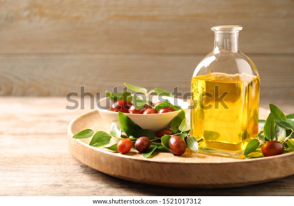 Glass bottle with jojoba oil and seeds on wooden\
table. Space for text