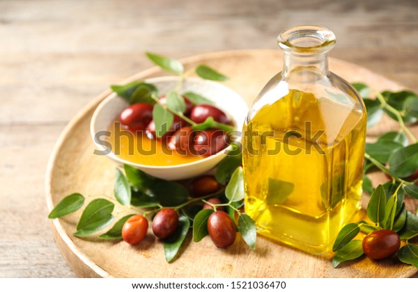 Glass\
bottle with jojoba oil and seeds on wooden\
table