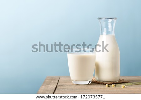 A glass and bottle of milk on wooden table with light blue background.