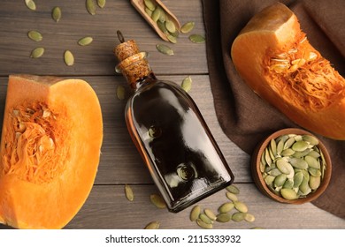 Glass bottle of oil with cut pumpkin and seeds on wooden table, flat lay