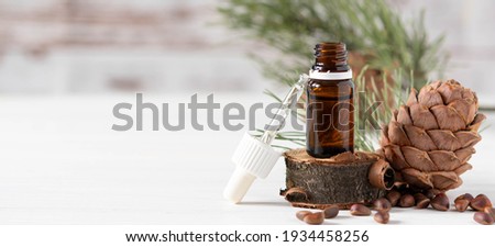 glass bottle with oil, pipette and cedar cone on light wooden background