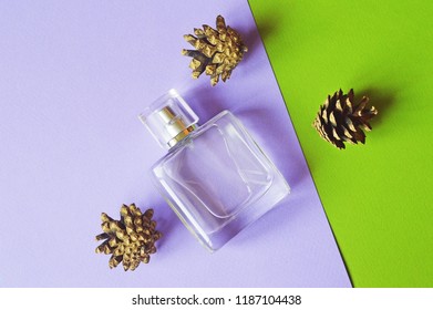 A Glass Bottle Of Perfume With A Woody Fragrance And Pine Cones On A Green And Purple Background Is A Top View. Flat Lay Beauty Photo For Cosmetic Shop