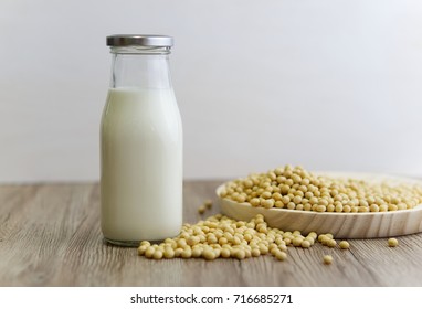 Glass Bottle Of Soy Milk With Spilled Container Of Soy Beans On A Light Brown Background