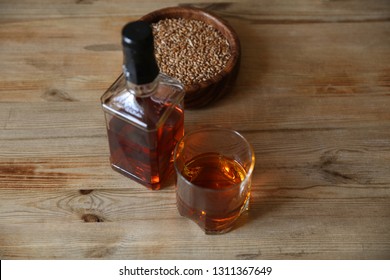 glass and bottle of whiskey with wheat in a bowl on wooden oak background with copy space for text