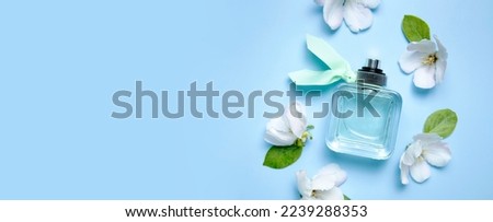 Glass bottle of women's perfume and spring flowers, green leaves on blue background. Perfumery, fragrance, cosmetics, natural spring fresh flower scent, toilet water. Flat lay top view 