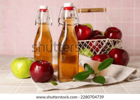 Glass bottles of fresh apple cider vinegar and basket with fruits on pink tile table Stok fotoğraf © 