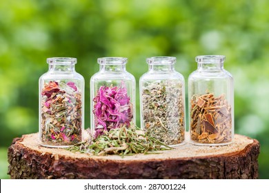 Glass bottles with healing herbs on wooden stump on green background, herbal medicine.