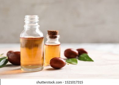 Glass bottles with jojoba oil and seeds on light table against grey background. Space for text