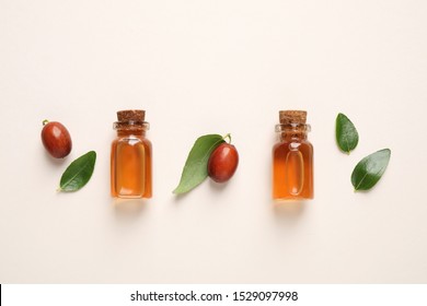 Glass bottles with jojoba oil and seeds on light background, flat lay