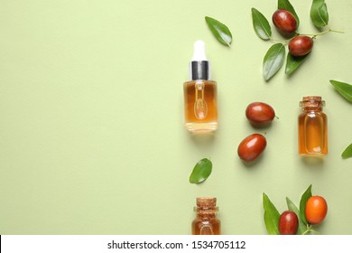 Glass bottles with jojoba oil and seeds on green background, flat lay. Space for text