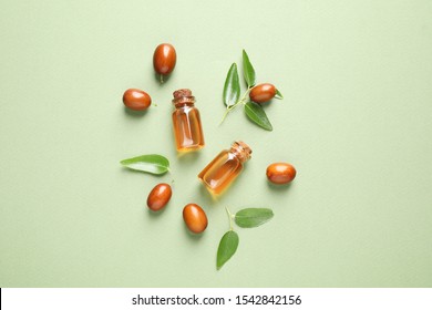 Glass bottles with jojoba oil and seeds on green background, flat lay