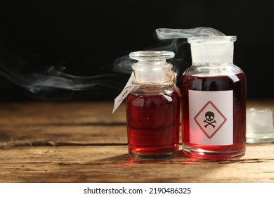 Glass Bottles Of Poison With Warning Signs On Wooden Table. Space For Text