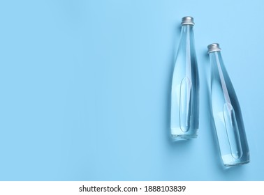 Glass Bottles With Water On Light Blue Background, Flat Lay. Space For Text