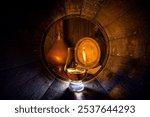 A glass of bourbon whiskey in old oak barrel. Copper alambic and oak barrel on background. Traditional alcohol distillery concept