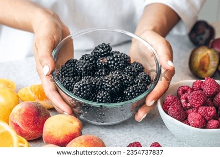 Glass bowl of blackberries in female hands in the kitchen.