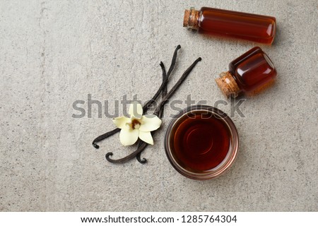 Glass bowl and bottles with vanilla extract on grey background