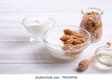 Glass Bowl With Greek Yogurt And Mixed Nuts. Healthy Sports Vegetarian Protein Rich Diet, Homemade Granola Breakfast With Milk, Honey, Almond, Cashew, Hazelnut, Rolled Oats. Top Front View, Background