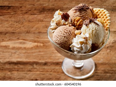 Glass Bowl Of Ice Cream Dessert With Chocolate, Nuts And Waffle, From Above Close-up On Wooden Background With Copy Space