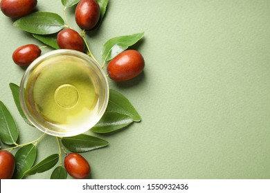 Glass bowl with jojoba oil and seeds on green background, flat lay. Space for text