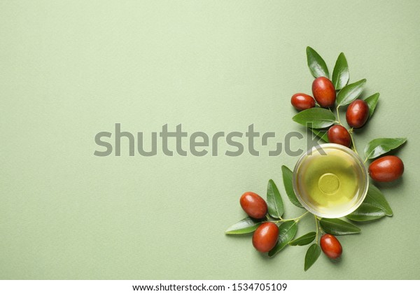 Glass bowl with jojoba oil and seeds on green\
background, flat lay. Space for\
text