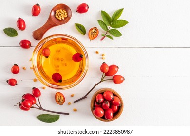 un recipiente de vidrio con aceite natural de semilla de rosa entre los frutos y hojas sobre una mesa blanca de madera. vista superior. un remedio natural. un espacio de copia