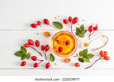 a glass bowl with organic natural rosehip seed oil among the fruits and leaves on a white wooden table. top view. antioxidant. a natural remedy