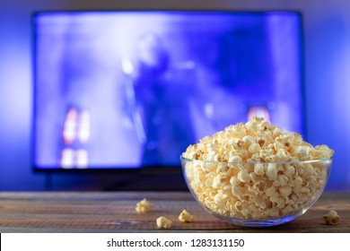 A Glass Bowl Of Popcorn And Remote Control In The Background The TV Works. Evening Cozy Watching A Movie Or TV Series At Home