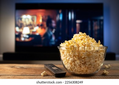 A glass bowl of popcorn and remote control in the background the TV works. Evening cozy watching a movie or TV series at home. - Powered by Shutterstock