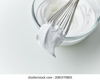 glass bowl of whipped egg whites cream on white kitchen table background, top view