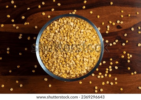 A glass bowl of yellow toor daal- pigeon peas scattered around on wooden table