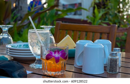 Glass With A Brightly Colored Mai Tai Cocktail At Dusk On A Table Set For A Luau