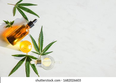 Glass brown bottle with cannabis oil with label and hemp leaves on a marble background. Copy space.