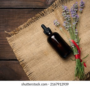 A glass brown bottle with a pipette and a bouquet of lavender on a brown wooden table. Container for cosmetic oils, serum