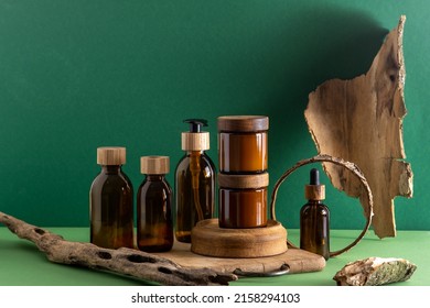 Glass brown containers for cosmetics with wooden lids. Cream jar, dropper bottle and lotion. Green background. Care and beauty. Bottles. Eco friendly concept. Cosmetic set box. Pipette and dispenser.
