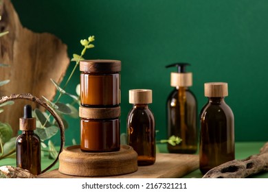 Glass brown containers for cosmetics with wooden lids. Cream jar, dropper bottle and lotion. Green background. Care and beauty. Bottles. Eco friendly concept. Cosmetic set box. Pipette and dispenser.