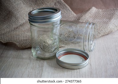 glass canning jars on a wooden table with burlap behing them.