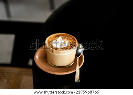Glass of cappuccino with latte art on saucer and with spoon on the black table. Breakfast drink