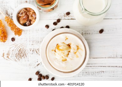 Glass Of Caramel Latte Coffee With Whipped Cream And Coffee Beans On A White Wooden Table, Top View
