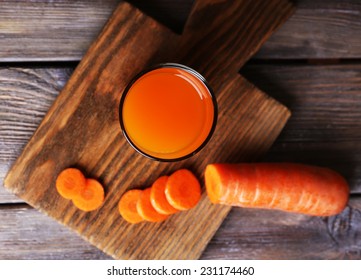 Glass of carrot juice and fresh carrot on cutting board on wooden table on wooden wall background