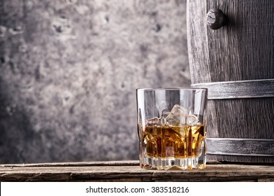 Glass and cask with old whiskey on wooden table