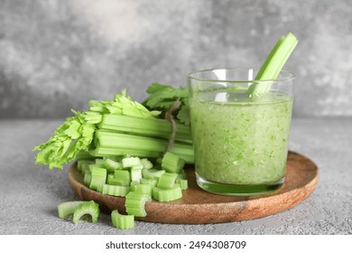 Glass of celery juice with chopped celery on grey background