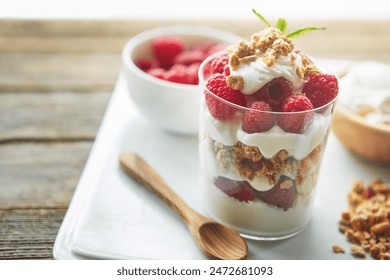 Glass, cereal and yogurt with raspberry with spoon for vegan food, organic or meal at breakfast. Fiber, dairy and fruit on plate by clear container with protein for morning, healthy nutrition or diet - Powered by Shutterstock