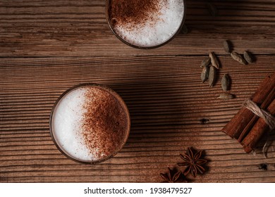 Glass of chai tea latte, hot latte foam garnish with ground cinnamon, drink with foamed milk on rustic wooden background, top view