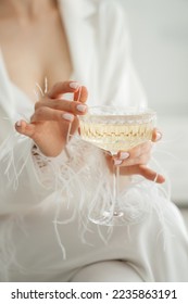 A glass of champagne in the hands of a beautiful bride in a white dress with pearls on the sleeves. Hands touch the glass. wedding drink.